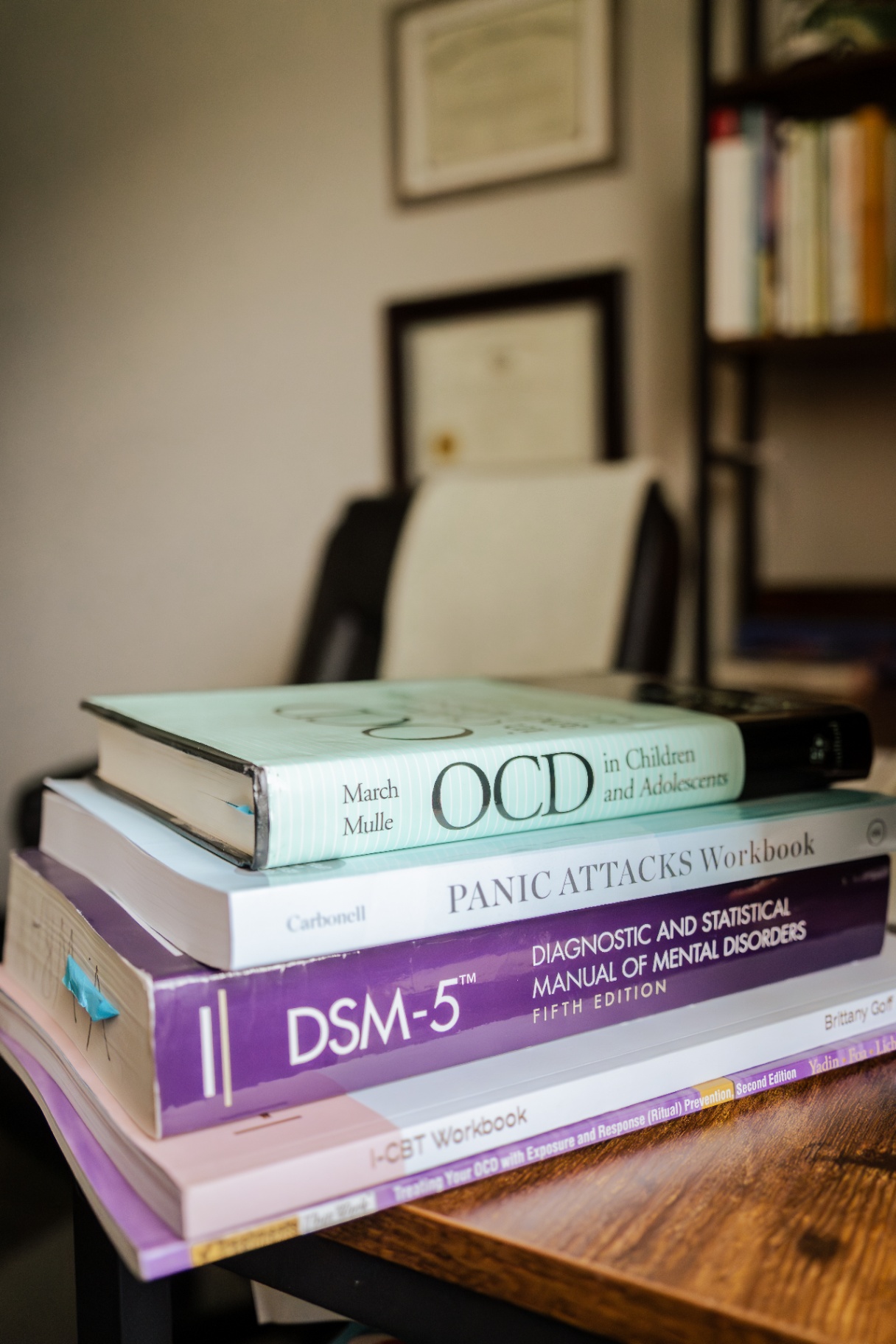 Stack of clinical reference books including DSM-5 and an OCD workbook on a therapist's desk