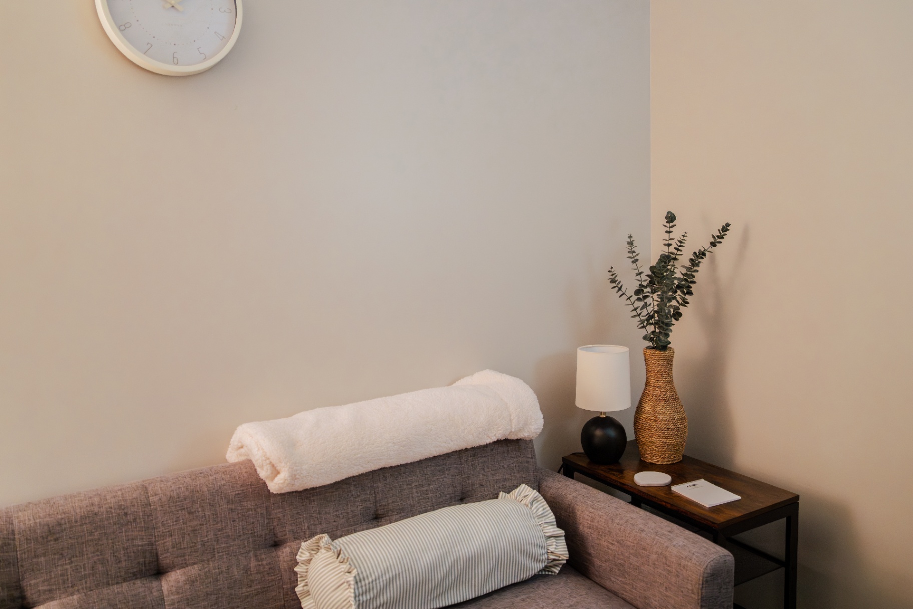 Calm therapy room with a soft grey couch, rolled blanket, eucalyptus branches, and a wall clock